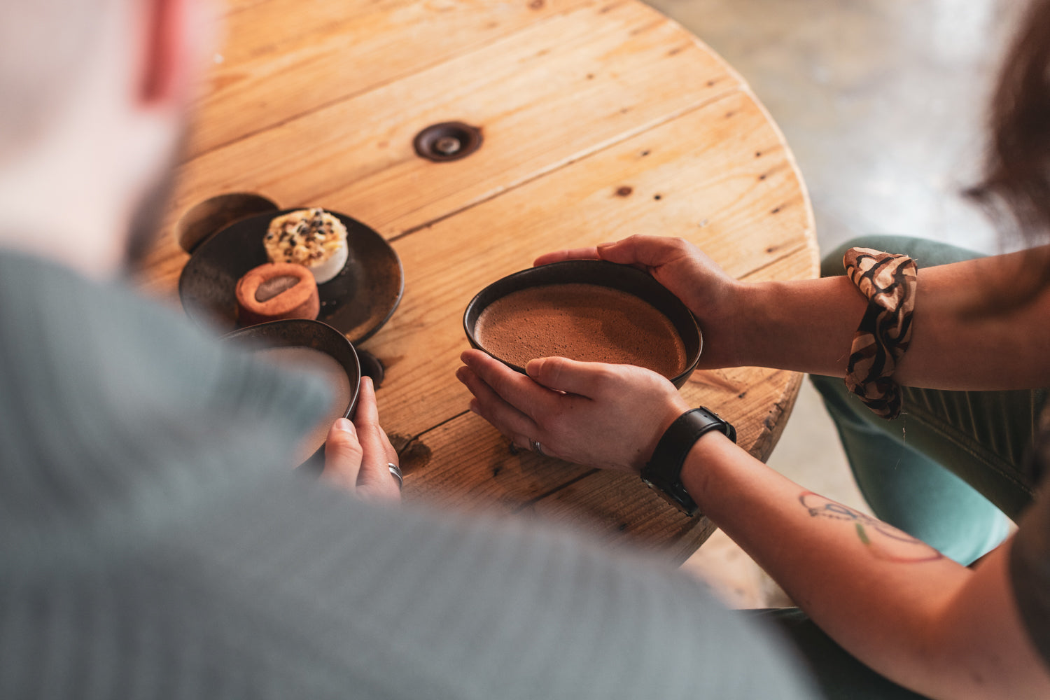 Hands around cups of Kakaw on a round wooden table