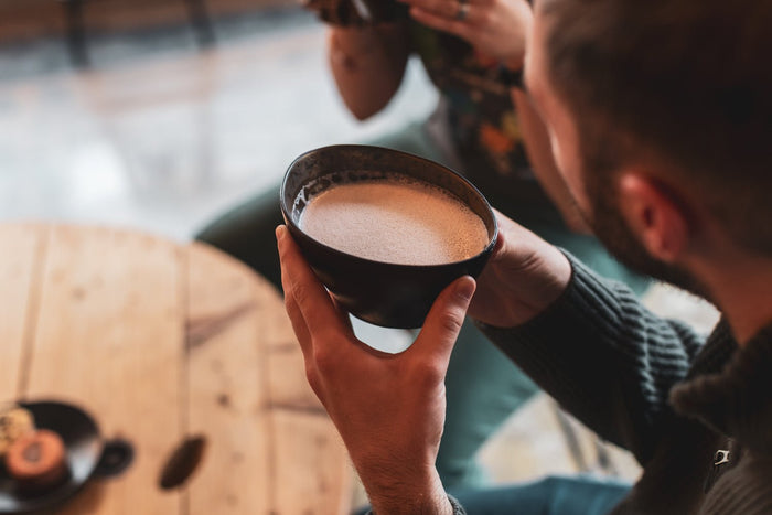 A man drinking Kakaw hot chocolate from a rustic black drinking cup